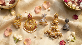 Five types of Indian bridal jhumka earrings including gold plated jhumka,  chandbali jhumka, floral AD jhumka, long dangler jhumka and oxidised jhumka  arranged on cream silk fabric with jasmine flowers for Indian wedding 2026