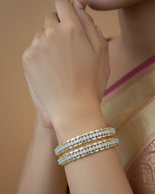 Close-up of a hand wearing two gold bangles on a blurred background