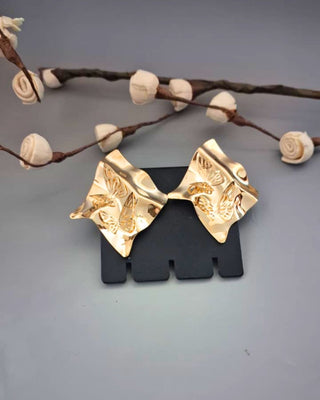 Gold earrings on a black stand with decorative branches in the background