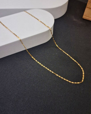 Gold chain on a dark surface with a white jewelry box in the background