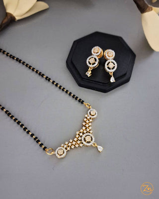 Gold necklace with black beads and matching earrings on a gray surface.