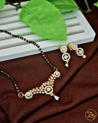 Gold necklace and earrings on a brown fabric background with green leaves.