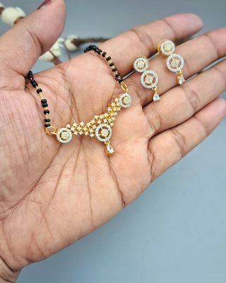 Gold necklace and earrings held in a hand against a neutral background