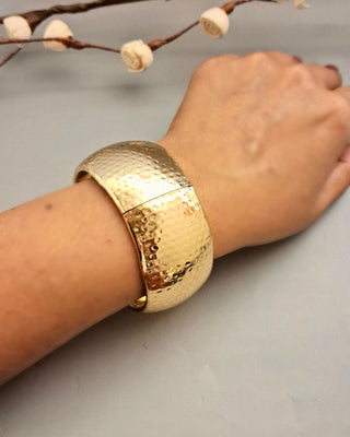 Gold bracelet on a wrist with a neutral background
