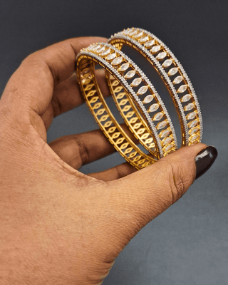 Gold bangles held in a hand against a dark background
