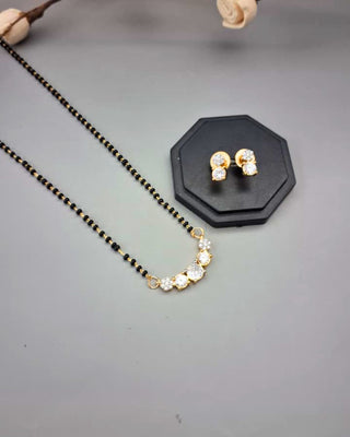 Gold necklace and earrings on a gray surface with a black stand.
