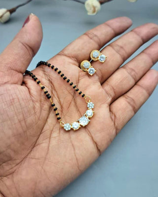 Hand holding a black beaded necklace and gold earrings with gemstones on a light blue background.