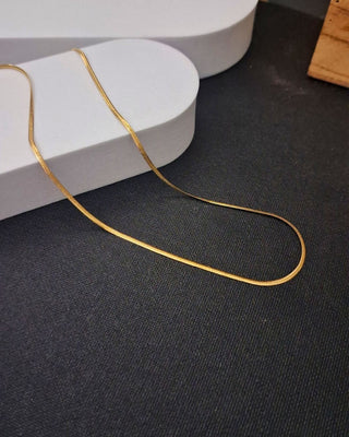 Gold chain on a dark surface with a white cylindrical object in the background
