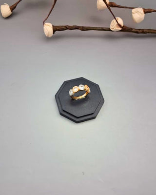 Gold ring with diamonds on a black stand against a gray background