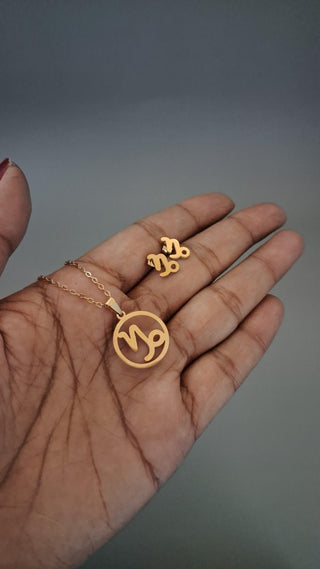 Gold necklace and earring set on a hand against a gray background