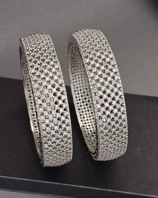 Two silver bangles with diamond-like stones on a dark background