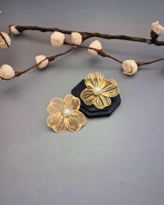 Gold flower-shaped earrings on a gray background with decorative branches.