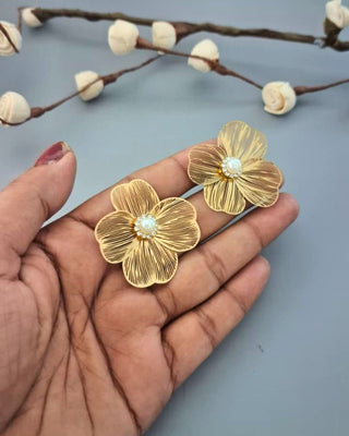 Gold floral earrings held in a hand with a light blue background