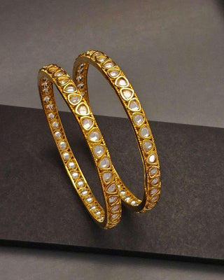 Gold bangles with pearl-like stones on a dark surface