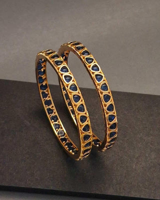 Gold bangles with blue stones on a dark surface