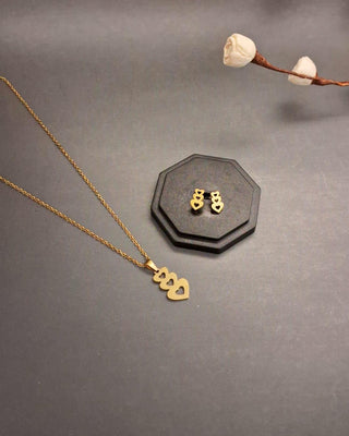 Gold necklace and earrings on a dark surface with a hexagonal black stand.