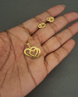 Gold heart-shaped necklace and earrings on a hand against a dark background