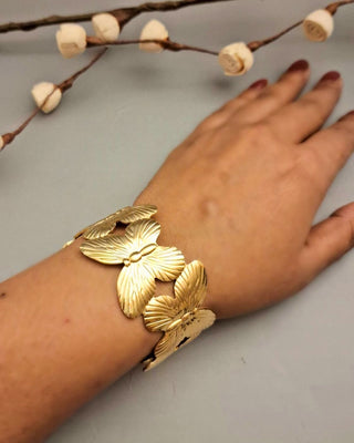 Gold butterfly bracelet on a wrist with a neutral background