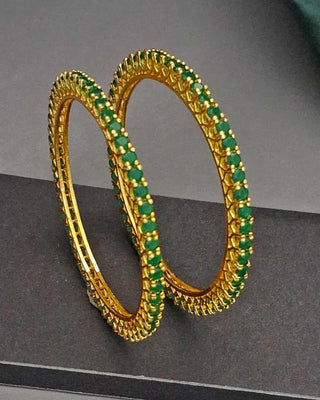 Gold hoop earrings with green gemstones on a gray background