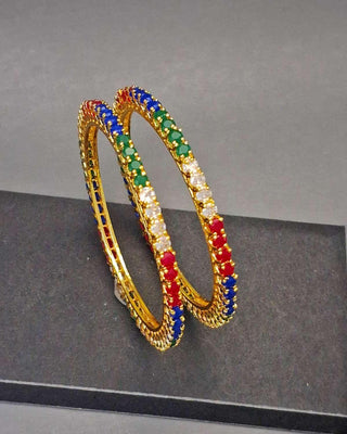 Gold bangles with colorful gemstones on a gray background