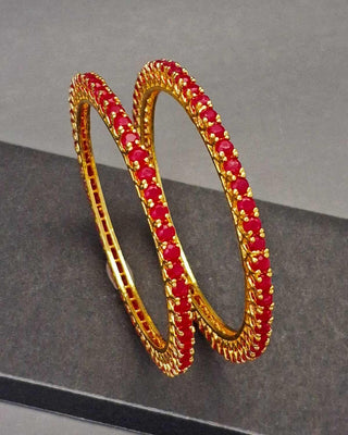 Gold hoop earrings with red gemstones on a gray background