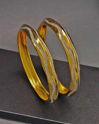 Two gold bangles on a dark surface with a gray background
