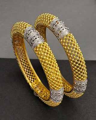 Pair of gold and silver bangles on a dark surface with a gray background