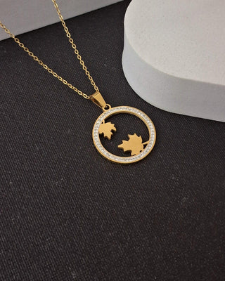 Gold necklace with a circular pendant featuring leaf designs on a black surface.