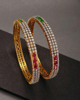Pair of gold bangles with gemstones on a dark surface