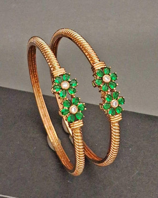 Gold bangles with green gemstones on a gray background