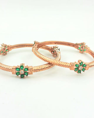 Rose gold bangles with green gemstones on a white background