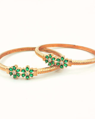 Two gold bangles with green gemstones on a white background