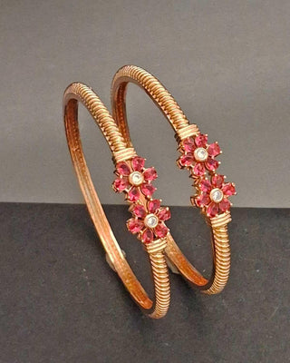 Rose gold bangles with pink gemstones on a gray background
