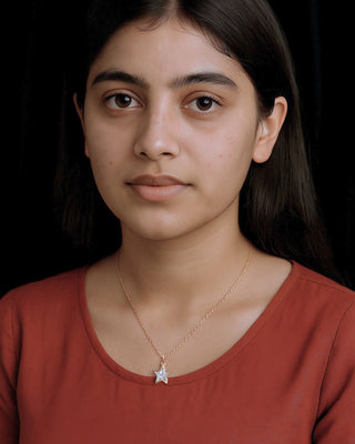Woman wearing a red shirt with a star pendant necklace against a black background
