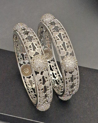 Pair of silver bangles with intricate designs on a dark surface