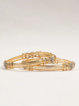 Set of gold bracelets with intricate designs on a light gray background