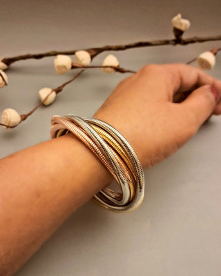 Hand wearing multiple gold bracelets with a neutral background