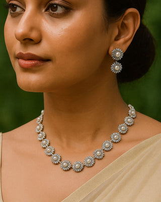 Woman wearing a floral pearl necklace and earrings with a blurred green background
