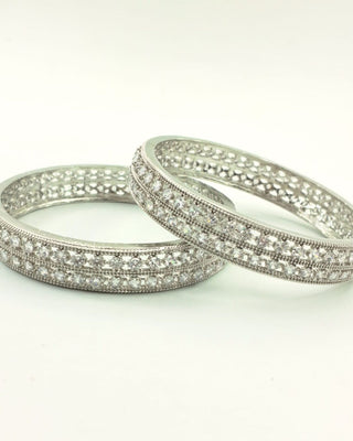 Two silver bangles with intricate designs on a white background