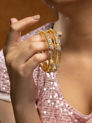 Gold bangles with gemstones held by a hand against a blurred background