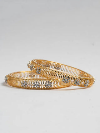 Gold bangles with diamond-like stones on a light gray background