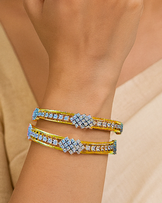 Close-up of a wrist wearing two Zevarly gold bangles with star cut cz gemstones on a beige background